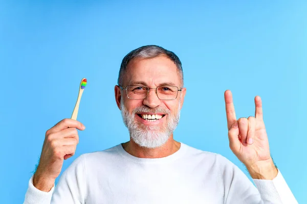 Man showing multi colored rainbow tooth brush in blue background studio — Stock Photo, Image