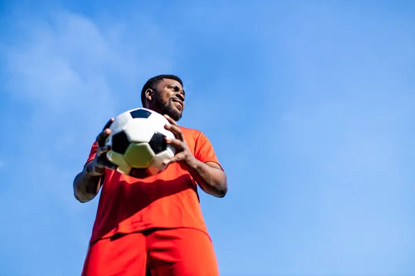 Feliz multicultural hispânico jogador de futebol sorrindo e usar terno esportivo vermelho ao ar livre dia ensolarado — Fotografia de Stock