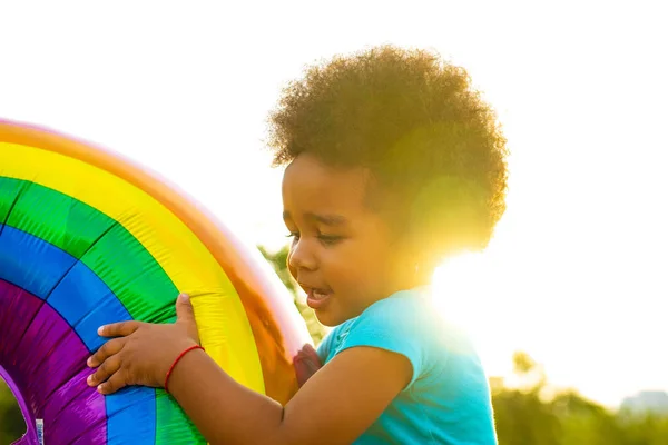 Bonito afro americano menina com cacheados afro cabelo jogando arco-íris balão ao ar livre — Fotografia de Stock