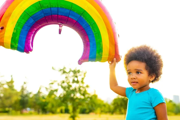 Süße afrikanisch-amerikanische kleines Mädchen mit lockigem Afro-Haar spielt Regenbogenballon im Freien — Stockfoto