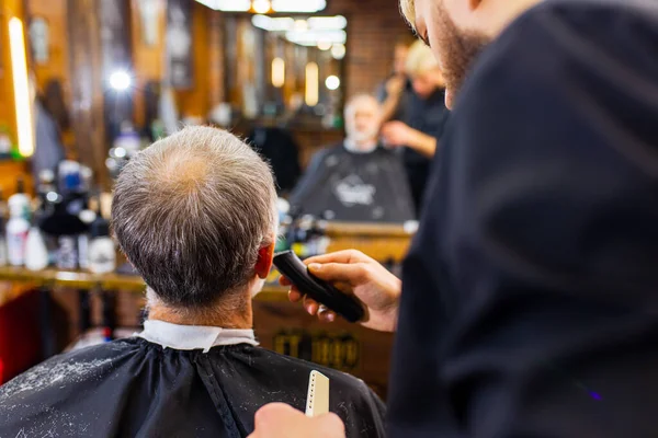 trendy stylish master cuts hair of old man client in modern barbershop