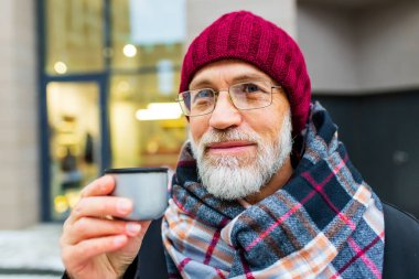 Yaşlı görünümlü adam kışın şehir caddesinde sıcak çay içer.