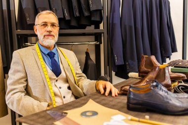 Gri sakallı yaşlı yakışıklı adam atölyede güzel bir takım elbise giyiyor.