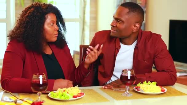 Αφρικάνικο ζευγάρι που τρώει ζυμαρικά ιταλικών τροφίμων στο σαλόνι σε κομψό σακάκι marsala χρώμα και πίνοντας κόκκινο κρασί — Αρχείο Βίντεο