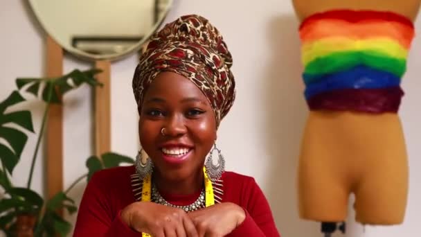 Tanzanian kobieta z węża druku turban nad usłyszeć tworząc kolorowe sukienki na paradę dumy w jej salon krawiecki — Wideo stockowe