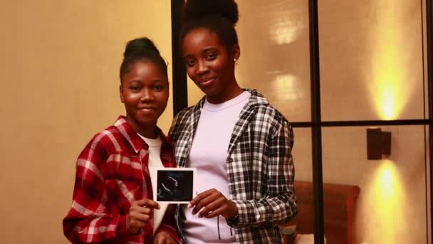 Afro-américain deux heureuses futures mères image échographie à la maison le soir — Video