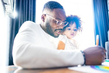 Otantik sakallı baba ve kız bebek masa ışığı arka planında resim çiziyorlar.