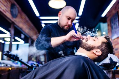 Berber dükkanında saçlarını buğulanmış nemli berbere kestiren İspanyol sakallı bir adam.