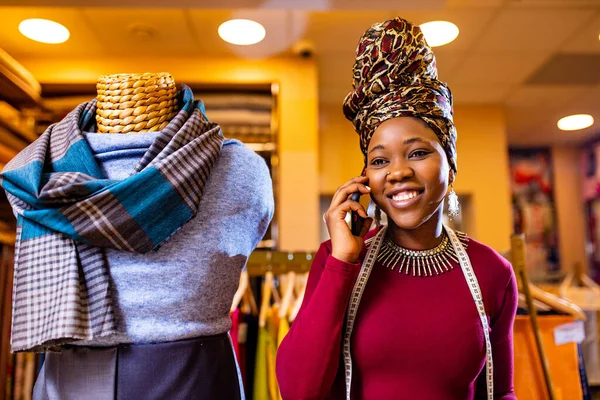 Tansanische Frau mit Turban mit Schlangenaufdruck hört Arbeit im Stoffladen per Smartphone beim Kunden anrufen — Stockfoto