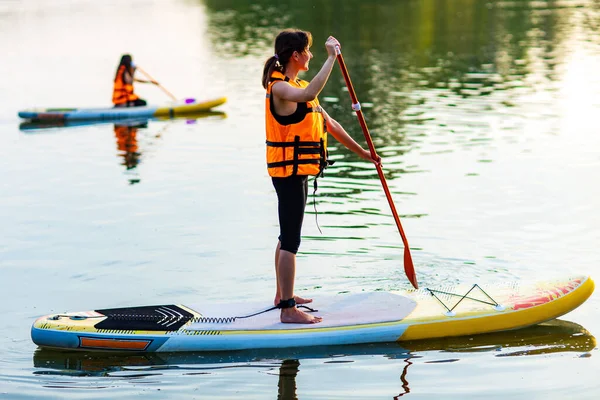 Jeune femme en gilet de sauvetage orange sur supboard à la rivière — Photo