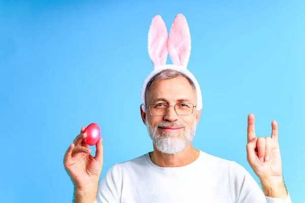 Bonito homem maduro com orelhas de coelho segurando ovo de Páscoa no fundo de cor azul — Fotografia de Stock
