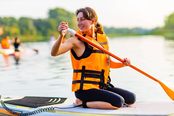 Young woman in orange life jacket on supboard at river — Stock Photo, Image