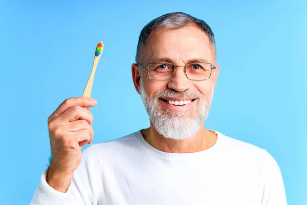 Hombre mostrando el cepillo de dientes de arco iris multicolor en estudio de fondo azul —  Fotos de Stock