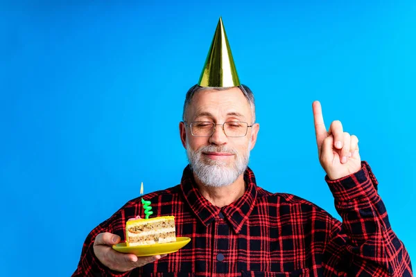 Man bär födelsedagshatt med tårta isolerad på klarblå färg bakgrund, studio porträtt — Stockfoto