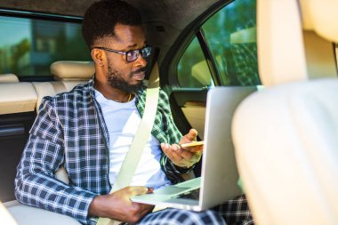Yakışıklı, başarılı, Afro-Amerikan iş adamları şık takım elbiseli, lüks bir arabada oturuyor ve dizüstü bilgisayarla çalışıyor.