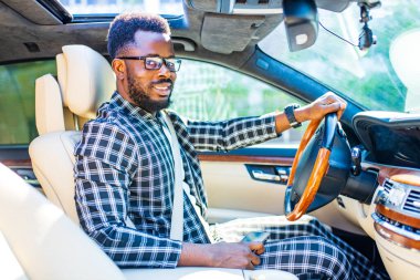 Şık ekose takım elbiseli Latin bir adam lüks spor arabalarda gözlük takıyor.