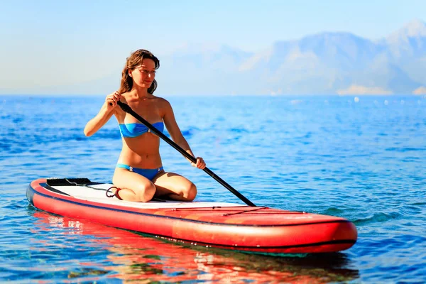 Frau paddelt auf Surfbrett mit Bergen im Hintergrund — Stockfoto