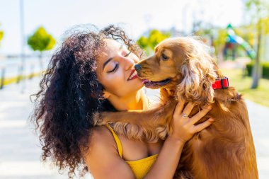 Neşeli, uzun, kıvırcık saçlı, Amerikan cocker köpeğiyle yaz parkında oynayan kadın.