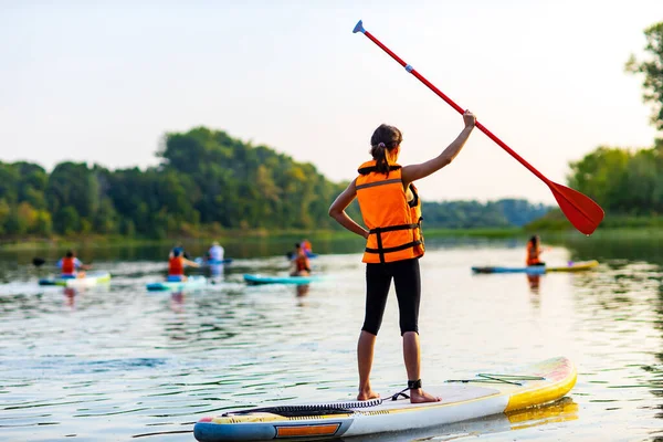 woman in life jacket at sub board at river ar evening , forest trees background