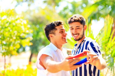 Mutlu eşcinsel çift yaz parkında cep telefonu kamerasıyla selfie çekiyor.