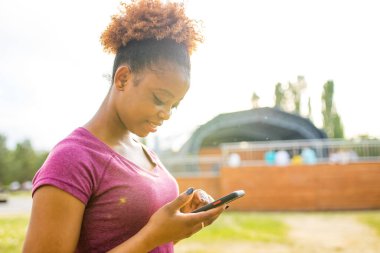 Pozitif gülümseyen kadın parktaki kablosuz interneti seviyor. Pembe elbiseler giyiyor..