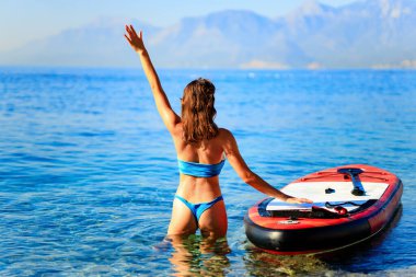 Arka planda dağlar olan bir kadın yemek masasında kürek çekiyor..