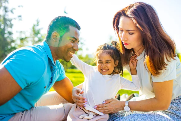 happy multicultural race family at picnic with food basket are sitting on plaid on the lawn.