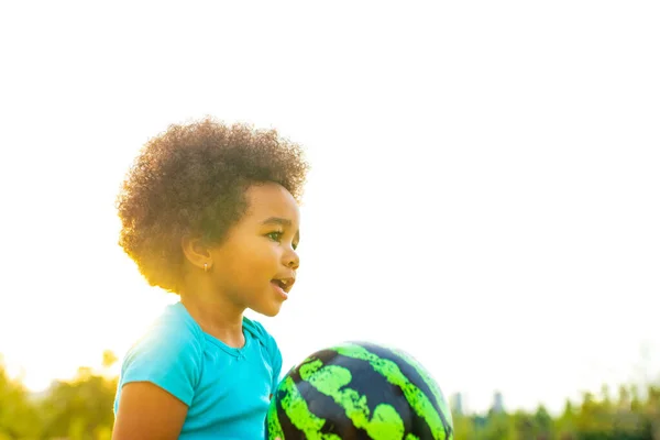 cheerful girl with afro curly hair playing with green ball like a watermelon outdoors .