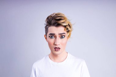 İğrenmiş Asyalı adam, lüks sarı saçları ve beyaz duvar arka planında muhteşem bir makyajı var..