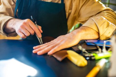 Yakışıklı bronz tenli usta terzi iş önlüğüyle kendi stüdyoda çalışıyor..