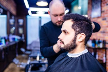 Arap yakışıklı sakallı adam berber dükkanında saçını kestiriyor..