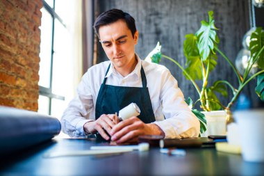 Hobi, önlüklü küçük bir iş adamı oldu. Deri bir cüzdan yapıyor ve stüdyoda şutluyor. .