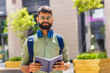 Güneşli bir günde mavi kulaklıklı ve sırt çantalı Hintli bir öğrenci.