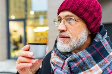 Yaşlı görünümlü adam kışın şehir caddesinde sıcak çay içer..