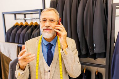 İyi giyimli, sakallı, olgun, yakışıklı adam atölyesinde müşterisiyle telefonla konuşuyor..