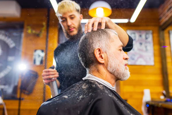 trendy stylish master cuts hair of old man client in modern barbershop.
