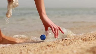 Bir kadın gönüllü, okyanus kıyısında plastik topluyor..