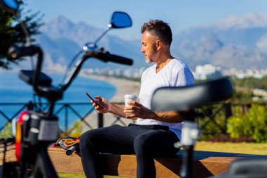 Yaşlı bir adam akıllı telefondaki uygulamayı kullanarak eko motorsikletle dışarıda takılıyor..