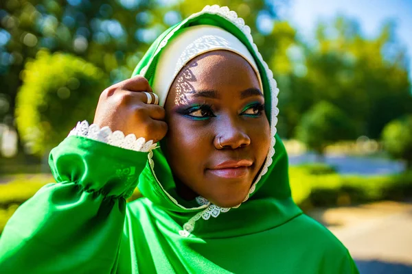 modern authentic multicultural race islamic woman in green cotton hijab with gorgeous make up outdoors in summer park.