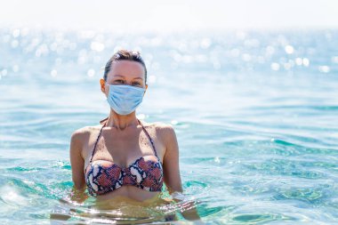 Güneşli bir günde yüzünde maskeyle suda yüzen paranoyak bir kadın..