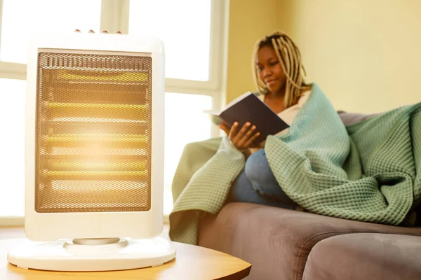 latin american woman with blanket reading a book in cold room with heater.