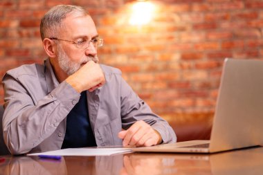 Gülümseyen orta yaşlı gözlüklü adam evde dizüstü bilgisayarla çalışıyor..