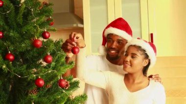 Latin çift evde kırmızı topla Noel ağacını süslüyor..