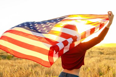 Sahada elinde yıldız ve çizgili bayrak tutan bir kadın altın gün batımında akşam güneşinde.