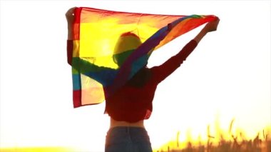Arazide elinde gökkuşağı lgbt bayrağı tutan bir kadın.