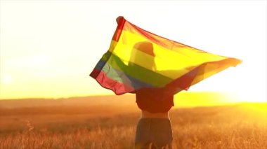 Arazide elinde gökkuşağı lgbt bayrağı tutan bir kadın.