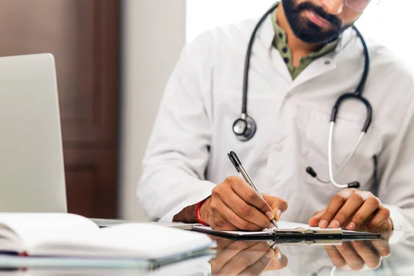 indian doctor wearing uniform taking notes in medical documents.
