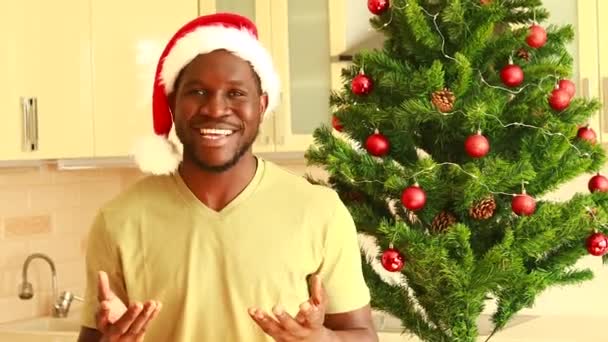 戴着圣诞礼帽的黑人在有圣诞树的房间里给摄像机带来好消息 — 图库视频影像
