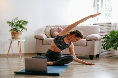 Spor yapan genç bir kadın kendi evinde yoga öğretiyor. Yogini 'nin canlı yayını, oturma odasındaki varyasyonları gösteriyor. İç arkaplan, kopyalama alanı, kapat.