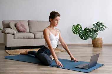 Spor yapan genç bir kadın kendi evinde yoga öğretiyor. Yogini 'nin canlı yayını, oturma odasındaki varyasyonları gösteriyor. İç arkaplan, kopyalama alanı, kapat.